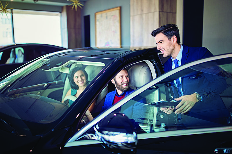 Car dealer is presenting a car to couple in the showroom